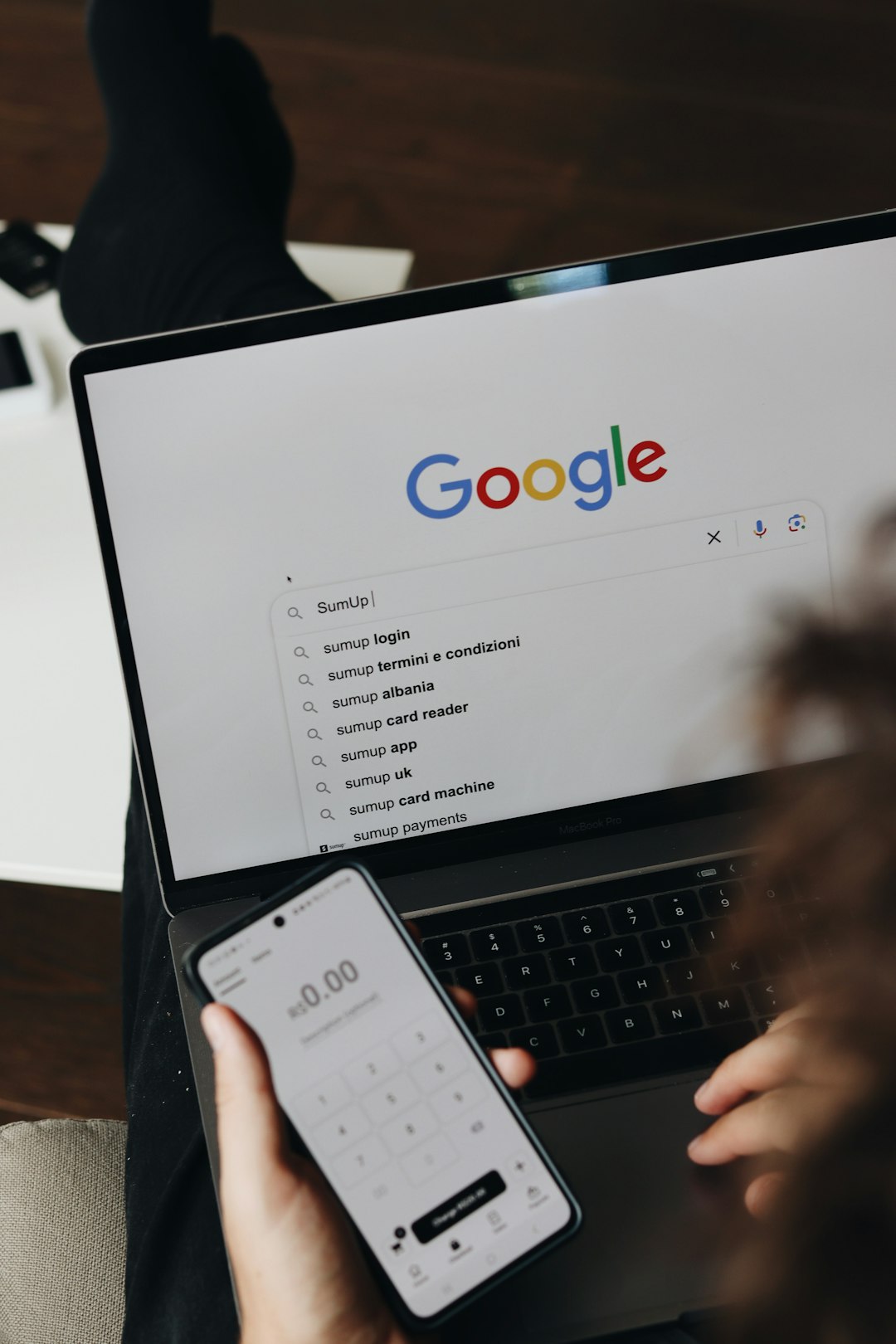 about-us A person is using a laptop to search for SumUp on Google while holding a white coffee mug. The Google search page is displayed on the screen, and the user is preparing to click Google Search.